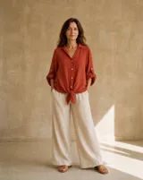 Camisa de lino color terracota, de corte holgado, con cuello camisero, cierre frontal de botones y mangas largas con detalles perforados y trabilla para arremangar.