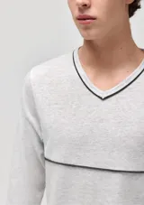 Pijama compuesto por una remera de manga larga con cuello en V y un pantalón largo de corte recto. La remera es de color gris claro con detalles de líneas oscuras en el cuello y el pecho, mientras que el pantalón es de color gris oscuro.