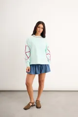 Buzo oversize de algodón con spandex, color verde menta, de manga larga con diseño de flores bordadas en rojo en las mangas y cuello redondo.