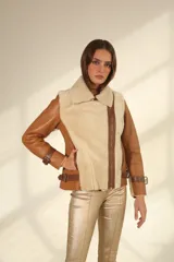 Chaqueta tipo gamulán de cuero color camel con interior y solapas de piel sintética en color beige. Presenta cierre frontal cruzado, correas ajustables con hebillas en los puños y en los laterales de la cintura.