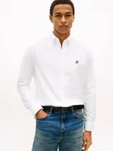 Camisa blanca de manga larga en tejido Oxford, de corte regular, con cuello abotonado y cierre frontal de botones. Cuenta con un pequeño logo bordado en el pecho.