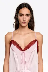 Vestido midi de corte recto confeccionado en una mezcla de acetato y viscosa. Presenta escote en pico con detalles de encaje, tirantes finos y un lazo decorativo en el centro del pecho. El diseño incluye tiras cosidas a lo largo de la prenda que aportan textura.