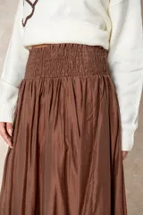 Pollera larga de estilo bohemio en color chocolate, confeccionada en tela satinada con caída fluida. Presenta un diseño de corte amplio con un volado en el ruedo y cintura elastizada para mayor comodidad.