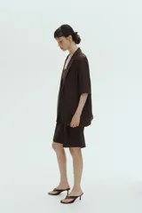 Blazer de manga corta color marrón oscuro, de botonadura sencilla con solapas de muesca, cierre de un botón, bolsillos delanteros ribeteados y forro interior.