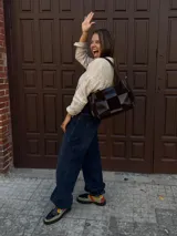 Cartera de hombro confeccionada en cuero y gamuza con diseño de damero, combinando paneles de texturas lisas y aterciopeladas. Presenta una manija trenzada y detalles de costuras artesanales en los laterales.