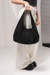 Bolso tipo hobo de gamuza negra, con diseño slouchy, costura vertical central y asa integrada para llevar al hombro.