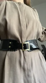 Cinto tipo faja ancho de cuero vacuno negro, con hebilla cuadrada dorada y detalles de costura trenzada en los bordes.