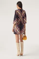Vestido corto de manga larga con estampado estilo paisley en tonos azul marino, rojo y crema. Presenta un escote redondo con cordones ajustables, cintura elástica y mangas abullonadas.