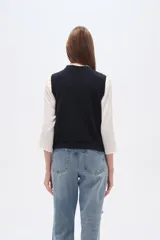 Chaleco de punto color azul marino, con cuello V y diseño de rombos trenzados. Presenta múltiples apliques bordados de motivos variados como mariposas, cerezas, flores, soles, lazos, limones, fresas, sonrisas, rosas y trozos de pizza.