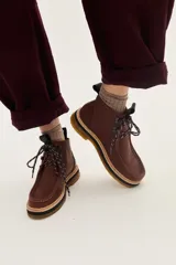 Borcego de cuero color marrón con diseño de costuras tipo mocasín en la puntera, cordones jaspeados y suela de goma con plataforma en capas.