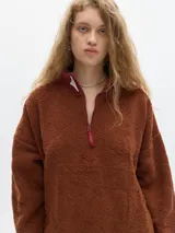 Buzo de fleece color marrón con cuello alto y cierre frontal de un cuarto. Presenta puños elásticos y un bordado en forma de rombo en el frente.