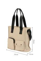 Bolso tipo tote color beige con doble asa superior negra y correa ajustable. Presenta un diseño estructurado con dos bolsillos frontales funcionales, uno con cierre y otro con solapa y broches a presión.