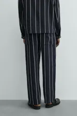 Pantalón de corte relajado, color azul marino, con rayas verticales blancas finas. Presenta cintura elástica ajustable con cordón interior y bolsillos laterales y traseros de plastrón.