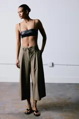 Pantalón culotte de tiro medio, con diseño de pierna ancha y pliegues frontales. Cuenta con cintura ajustable mediante cordones, bolsillos laterales y cierre frontal con cremallera y gancho metálico.