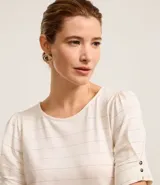 Blusa de viscosa texturizada color beige, con rayas horizontales en hilo metalizado, cuello redondo y mangas cortas con botones.