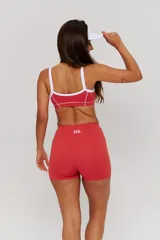 Conjunto deportivo compuesto por un top y un short de tiro alto en color bordó con detalles de líneas blancas. El top presenta breteles anchos y el logo de la marca en el frente, mientras que el short tiene un diseño ajustado con costuras laterales visibles.