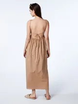 Vestido largo blanco de algodón con escote en V, breteles finos regulables y espalda descubierta con lazo para atar. Presenta un diseño holgado con bolsillos laterales.