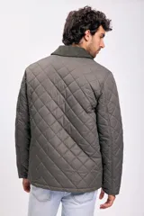 Campera capitonada de color verde oliva, con cierre frontal mediante botones a presión y cuello de pana en tono contrastante. Presenta un diseño acolchado con patrón de rombos y bolsillos laterales.