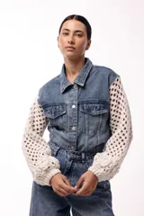 Campera de jean con cuerpo de denim clásico y mangas largas tejidas en crochet color crema. Presenta diseño de red en las mangas con detalles de flores tejidas en relieve en los puños, cuello camisero y cierre frontal con botones metálicos.