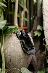 Sandalias negras con diseño de tiras, combinando cuero liso y textura efecto cocodrilo. Poseen suela track con plataforma y cierre de hebilla en el tobillo.