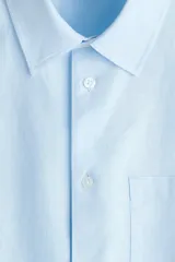 Camisa en mezcla de lino y algodón color celeste, de corte relajado, manga larga, con cuello inglés, bolsillo frontal y cierre de botones.