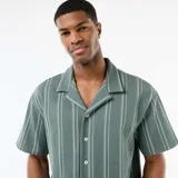 Camisa de manga corta de color verde con diseño de rayas verticales blancas, cuello tipo cubano y cierre frontal con botones.