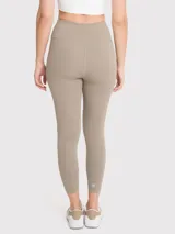 Calza deportiva de tiro alto con largo al tobillo, confeccionada en tejido elástico de color beige. Presenta un diseño minimalista sin bolsillos y un pequeño logo bordado en la cadera.