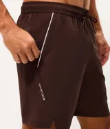 Bermuda deportiva de corte corto, color marrón oscuro, confeccionada en tejido técnico liviano y de secado rápido. Cuenta con cintura elástica con cordón de ajuste y bolsillos laterales con detalle de vivo contrastante.