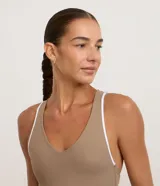 Enterito deportivo corto color marrón topo, ajustado al cuerpo, con escote en V pronunciado y breteles finos blancos que se cruzan en la espalda.