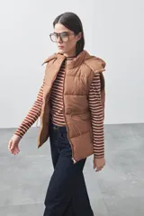 Chaleco puffer negro con diseño acolchado, capucha desmontable y cierre frontal. Cuenta con cordones ajustables en la cintura y bolsillos laterales.