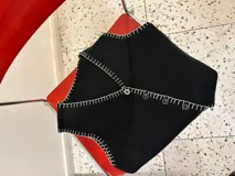 Chaleco tejido color negro con corte sastrero y abotonadura frontal. Presenta un bordado a mano en hilo blanco en todo el contorno de la prenda, incluyendo cuello, sisas y borde inferior.