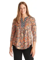 Blusa de seda fría estampada con motivo floral paisley en tonos naranja, negro y beige. Cuello a la base con escote en V y patrón geométrico. Corte holgado con fruncido bajo el pecho y mangas tres cuartos. Ruedo con aberturas laterales y terminación redondeada.