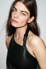 Top de cuello halter con hebilla metálica ajustable, diseño sin mangas y espalda descubierta. Presenta frunces laterales que crean un efecto drapeado y un bajo asimétrico. Cuenta con cierre lateral con cremallera oculta.