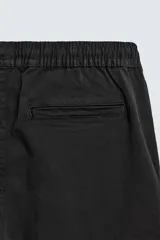 Pantalón cargo de corte slim fit en color negro, confeccionado en tejido de algodón con elasticidad. Presenta cintura elástica ajustable con cordón, bolsillos laterales tipo cargo con solapa y bajo acabado en puño elástico.