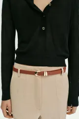 Pantalón tobillero de tiro medio, color azul marino, con bolsillos delanteros y cierre frontal con cremallera, botón y gancho. Incluye un cinturón fino de color marrón con hebilla metálica.