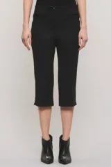 Pantalón capri negro de corte sastrero, confeccionado en tejido de punto grueso con elastano. Presenta calce slim, alforzas en el delantero, bolsillos ojal simulados, aberturas laterales en los bajos y cierre frontal con botón y broche metálico.