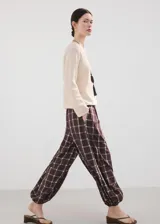 Pantalón balloon de tiro medio en color marrón oscuro con estampa de cuadros. Cuenta con cintura ajustable con goma y cierre de lazo, además de dos bolsillos laterales y diseño abuchonado en los tobillos.