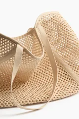 Bolso de playa de red color beige, confeccionado en paja plástica con dos asas largas y base rígida.
