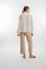 Camisa de manga larga color blanco marfil con patrón de rayas diagonales semitransparentes, cuello camisero, cierre frontal con botones y mangas abullonadas con puños ajustados.