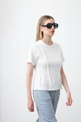 Remera de manga corta y cuello redondo, confeccionada en algodón. Presenta costuras verticales visibles en el frente que generan un efecto de entalle y estructura en la cintura.