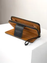 Billetera grande de cuero negro con textura de reptil y detalles de costuras en contraste. Cuenta con solapa frontal con cierre magnético y correa de muñeca extraíble.