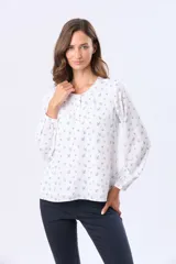 Blusa de manga larga con cuello redondo y cierre frontal de botones. Presenta un estampado floral en color negro sobre fondo blanco.