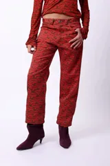 Pantalón de corte recto y largo al tobillo, con estampado geométrico en tonos oscuros y líneas rojizas. Posee tiro medio y cierre frontal.