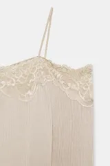 Camiseta color beige de escote recto y hombros descubiertos, con tirantes finos y manga larga. Presenta un detalle de encaje a tono en el escote y está confeccionada en tejido rib.