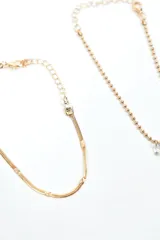 Set de cuatro pulseras doradas de diferentes diseños: una con cristales incrustados, una fina con dijes colgantes, una de cadena tipo víbora y una de cadena gruesa con un dije de corazón pavé.