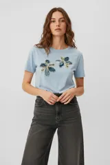Remera de algodón color celeste con cuello redondo y mangas cortas. Presenta apliques decorativos en el frente con diseño de flores bordadas y detalles de lentejuelas.