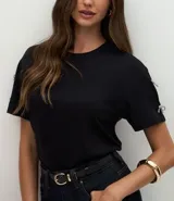 Camiseta blanca de algodón con cuello redondo y mangas cortas, decorada con pequeños lazos brillantes en los laterales de las mangas.