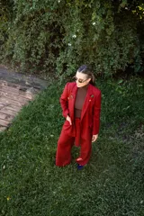 Blazer de corte sastrero con estampado cuadrillé en tonos rojos y negros, con solapas clásicas y cierre frontal. Presenta detalles de pines decorativos en las solapas.
