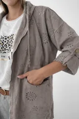 Campera fina de algodón color gris topo con capucha y cierre frontal. Presenta detalles tipo broderie, corte holgado y mangas con opción de remangar.