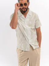 Camisa de manga corta rústica en tono verde militar con estampado abstracto claro, cuello cubano y cierre frontal de botones.